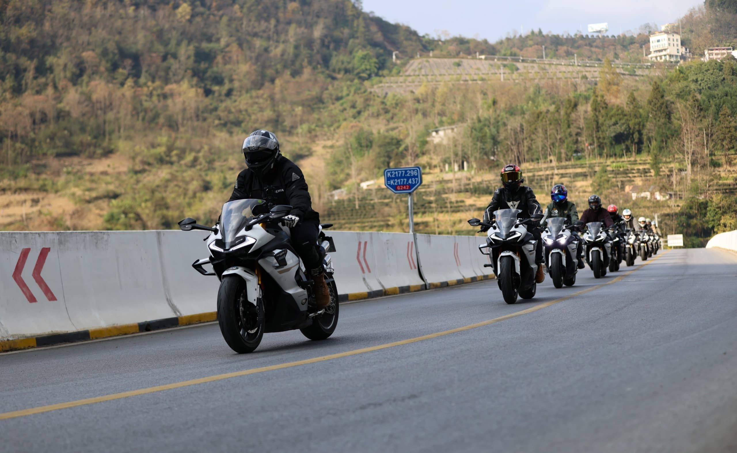 A line of motorcyclists in full gear riding on a scenic mountain road.