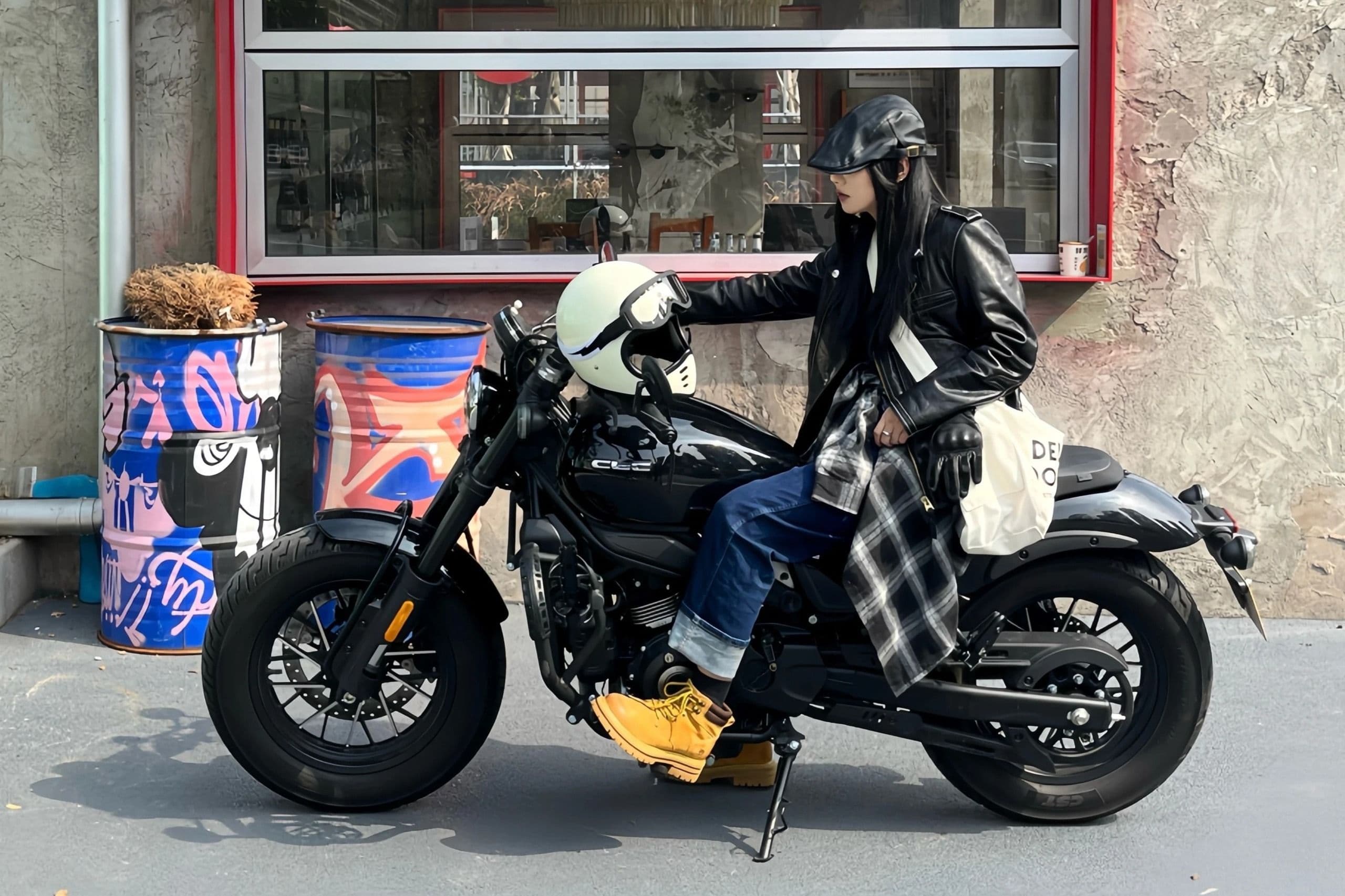 Woman in black leather jacket and helmet sits on a black motorcycle.