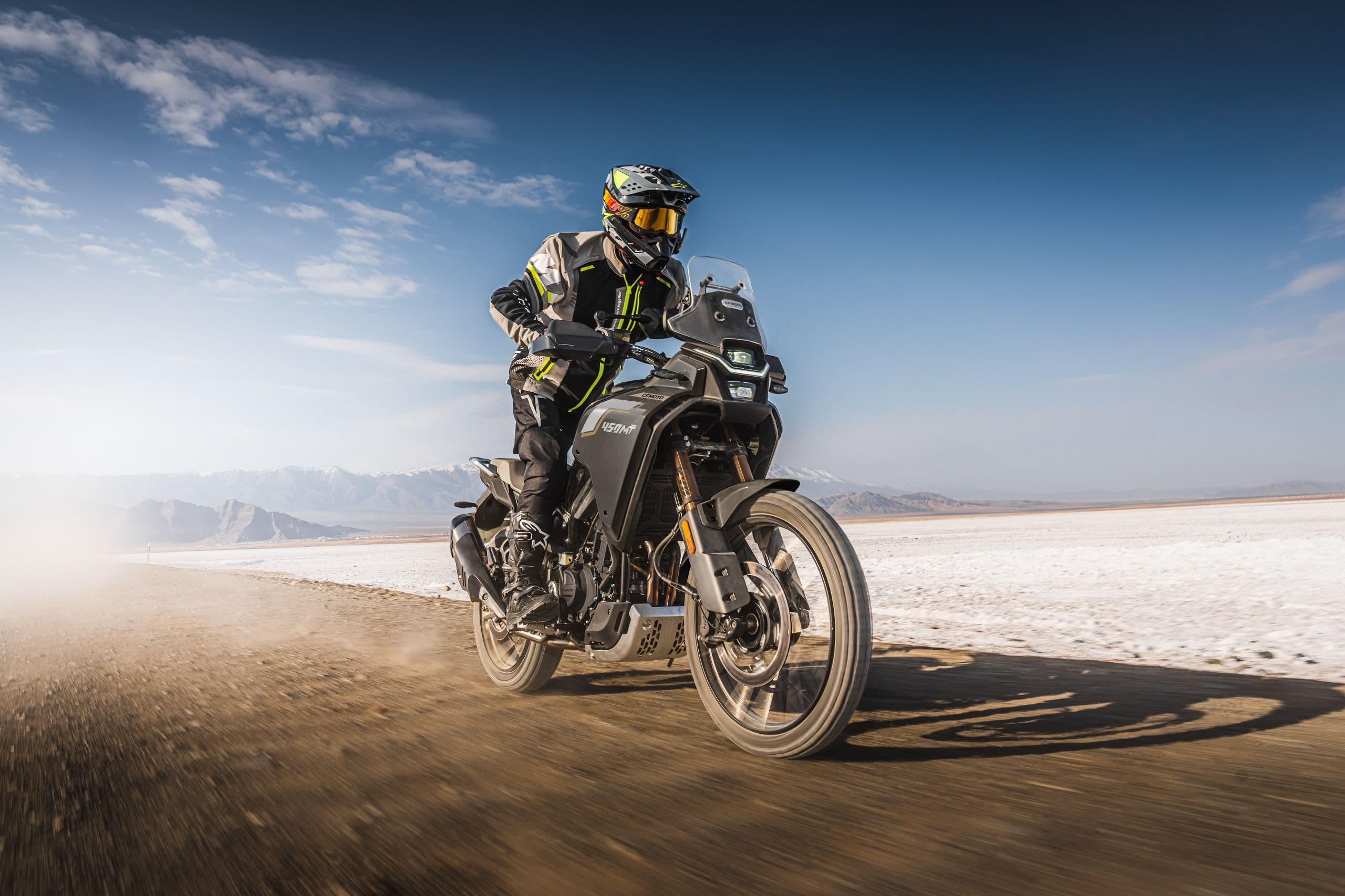 Rider on a black motorcycle kicking up dust while riding fast on a dirt road.