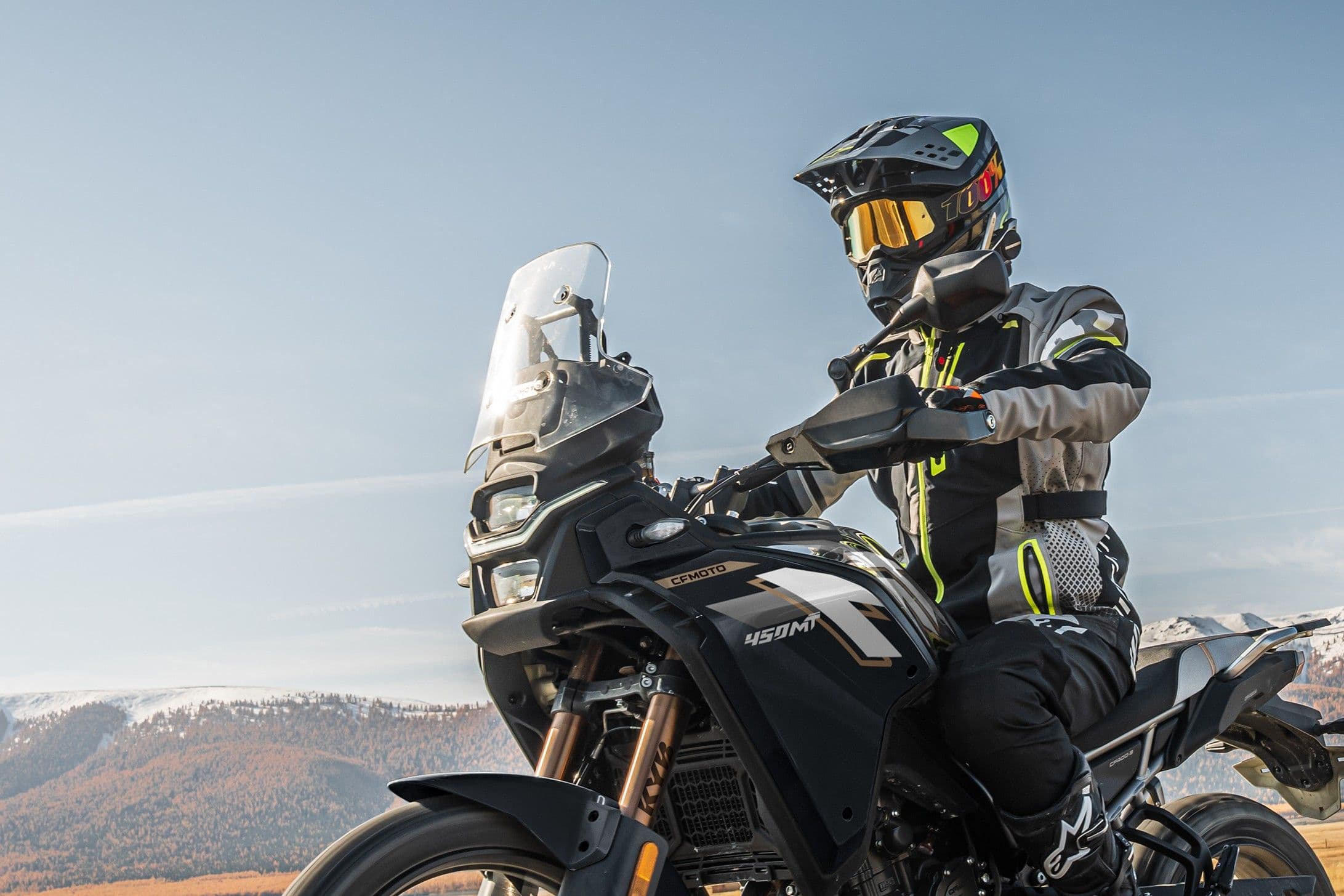 Rider on a black adventure motorcycle wearing a helmet, looking forward on a sunny day.