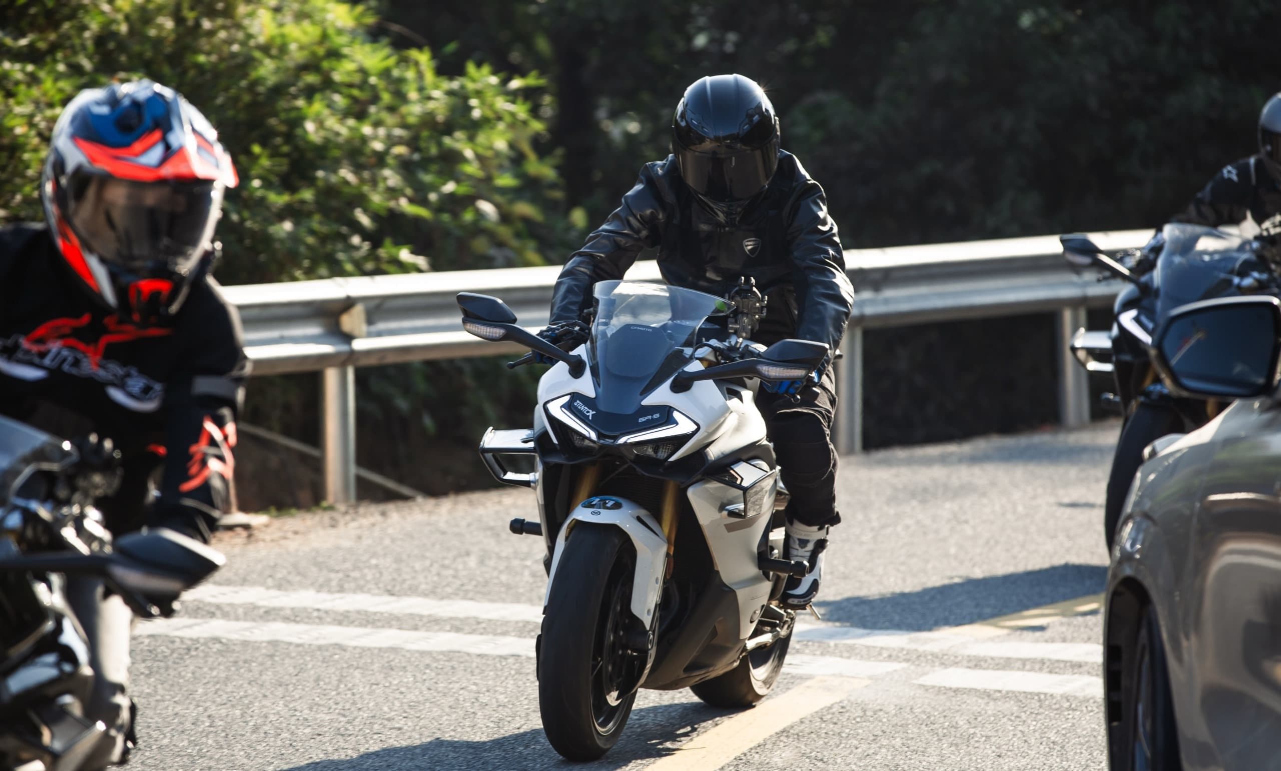 A person in black gear rides a white and black sport motorcycle on a winding road.