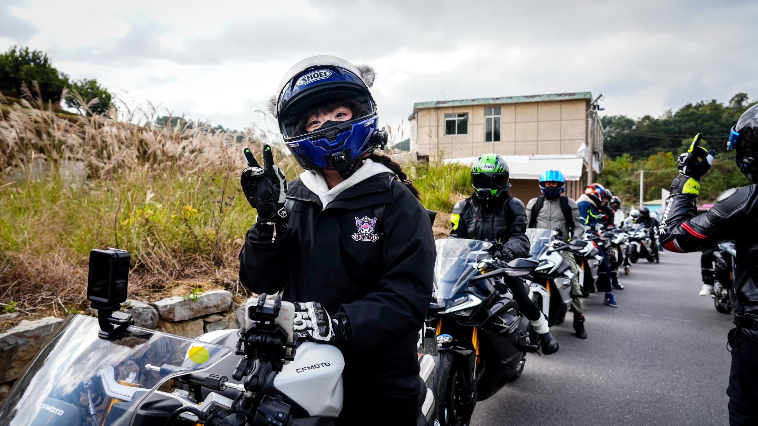A motorcyclist in a blue helmet makes a peace sign with other riders.