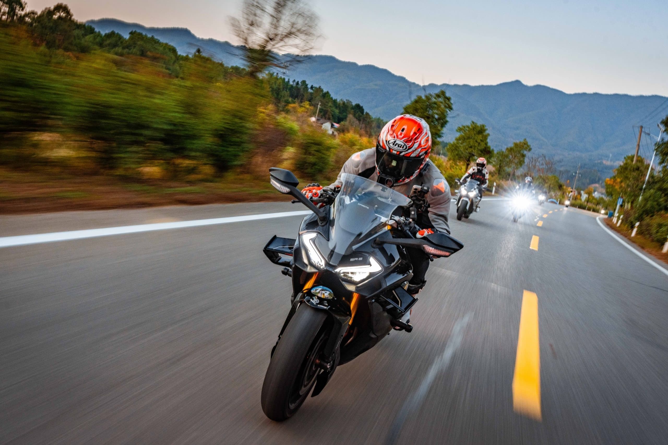 Two motorcyclists lean into a turn on a winding mountain road at dusk.