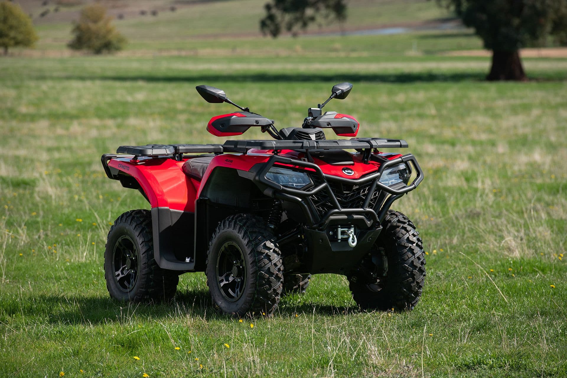 Red ATV parked on a green grassy field under a bright sky.