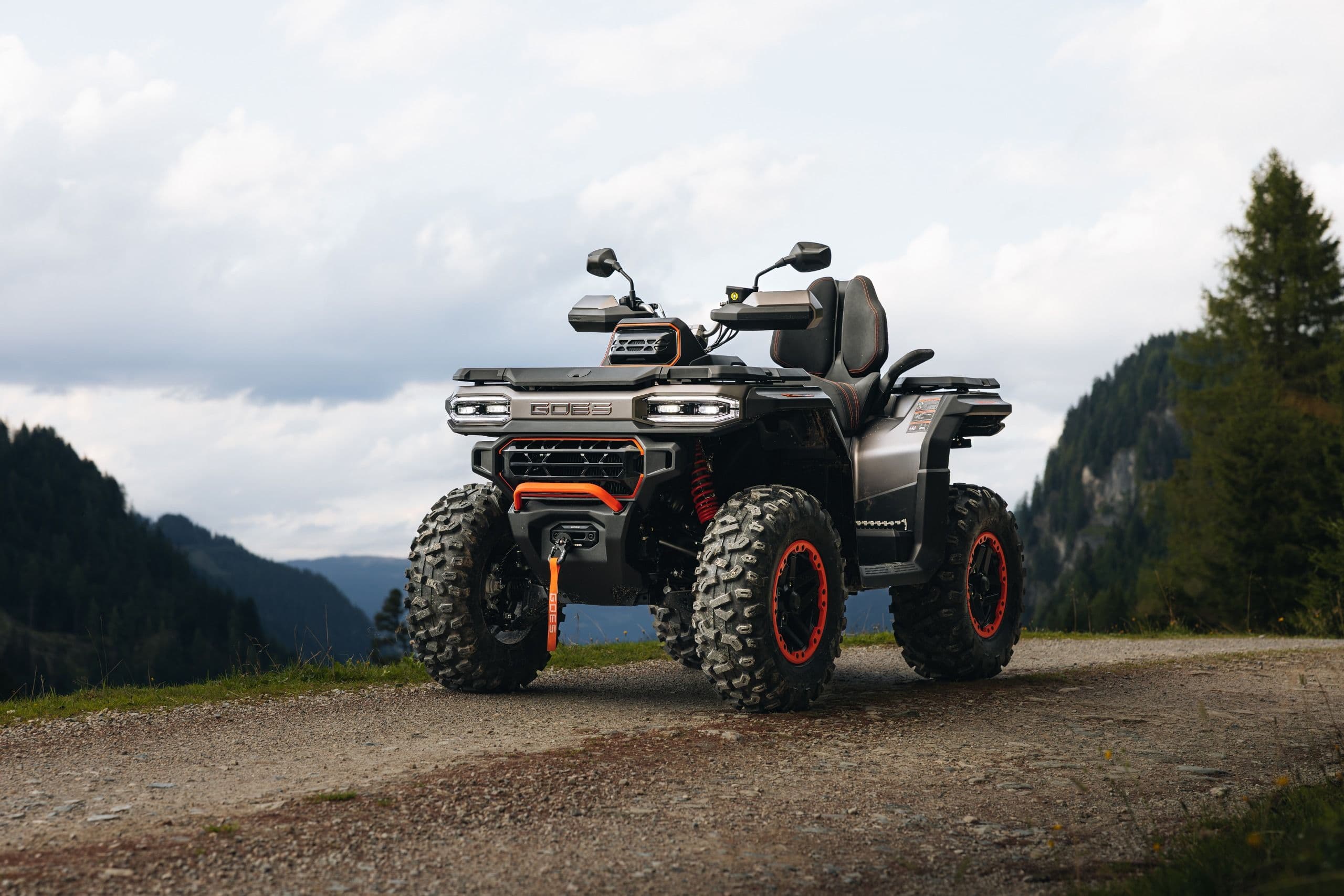 Grey ATV parked on a dirt road, with mountains and trees in the background.