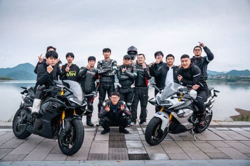 A group of male motorcyclists poses with their bikes next to a lake.