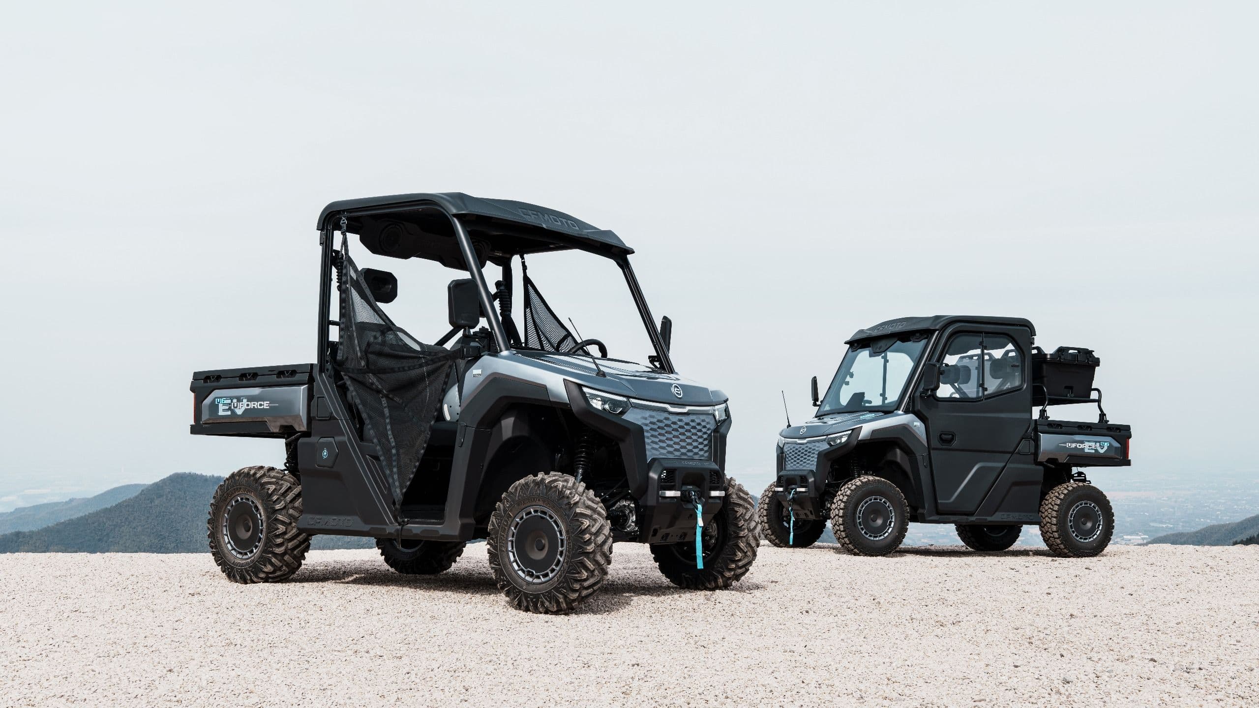 Two gray utility vehicles, different sizes, parked on a dirt road.