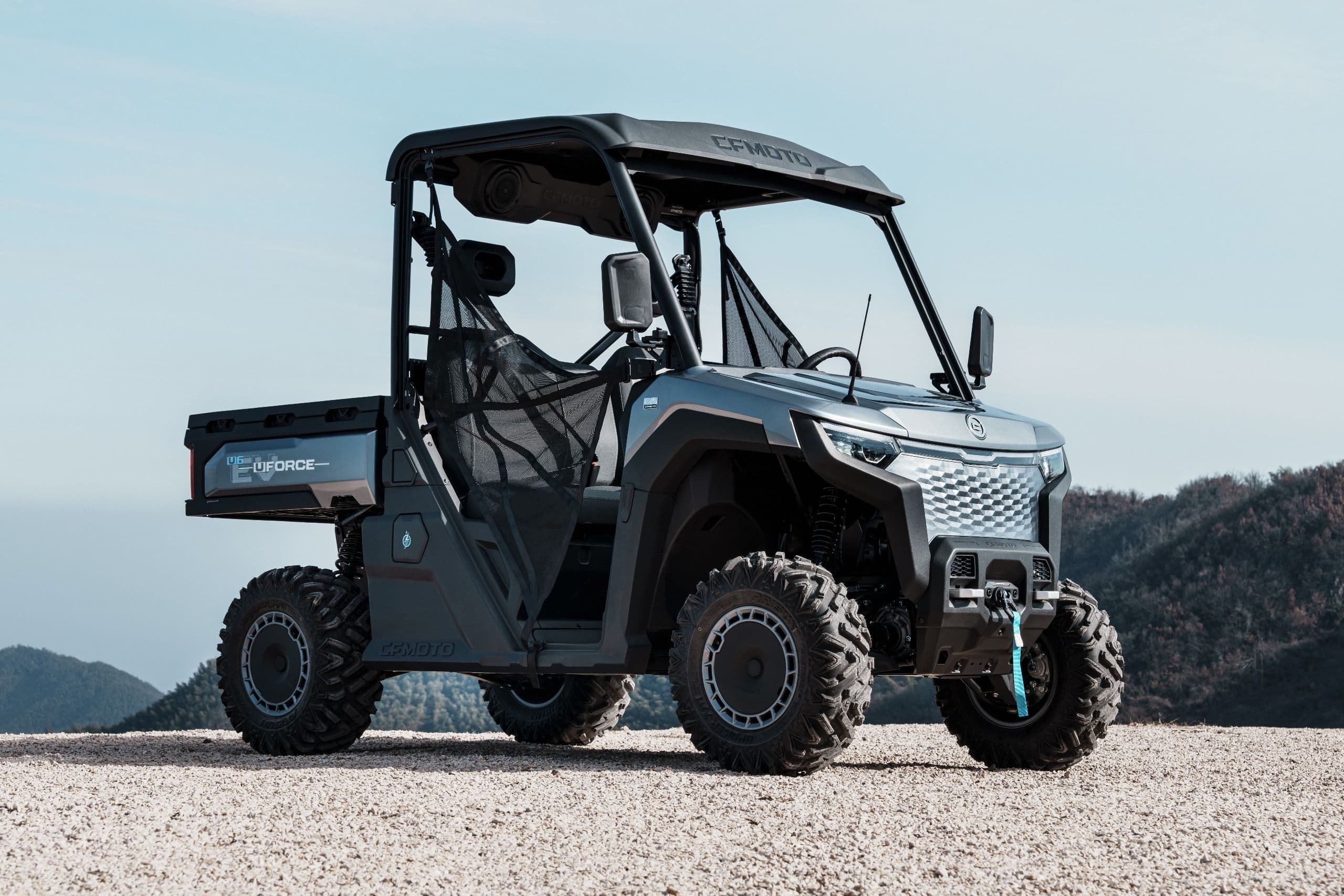 Gray UTV parked on a dirt hill under a clear blue sky and mountains.