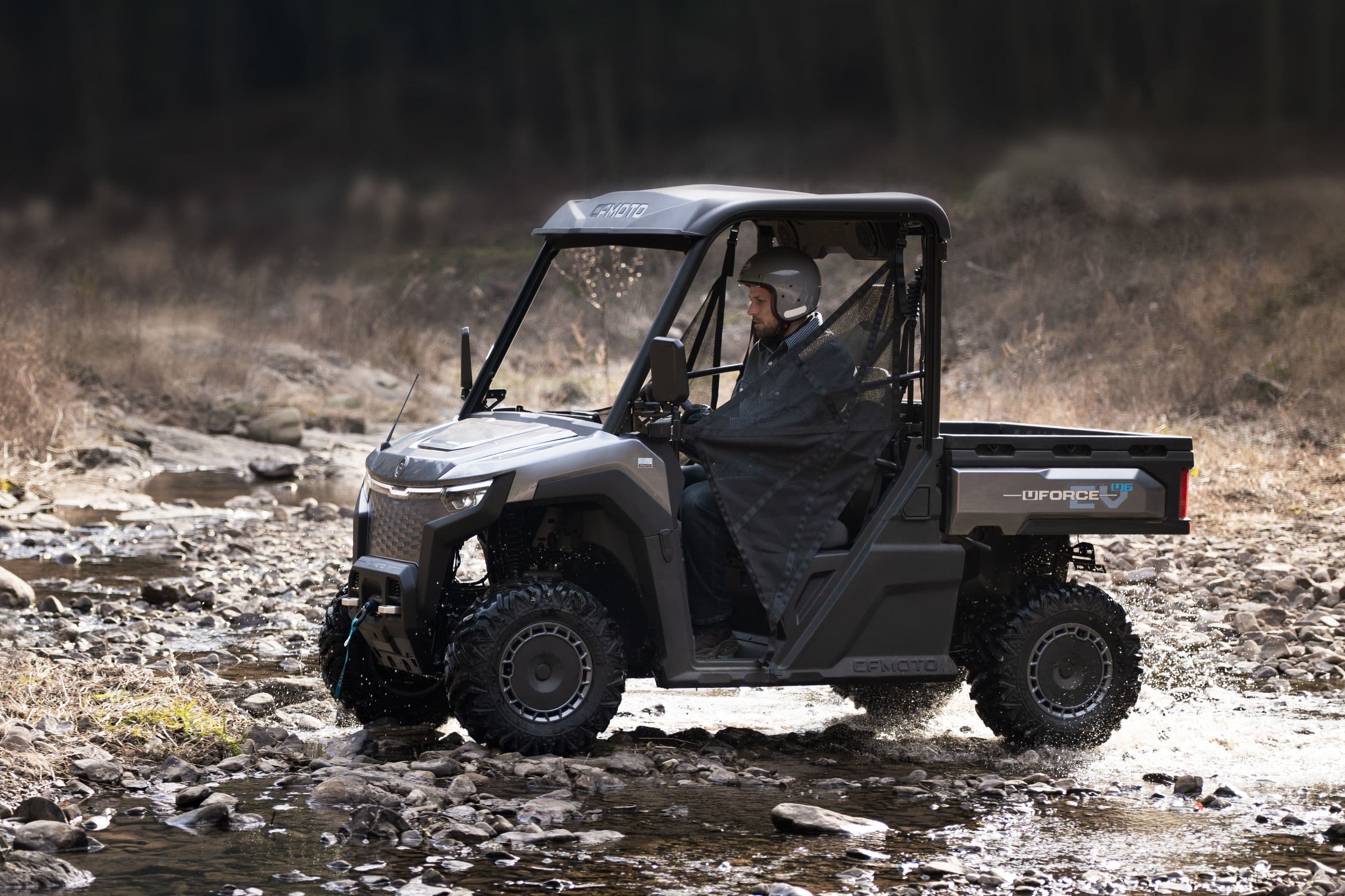 Gray UTV driven by a person splashes through water on a muddy trail.