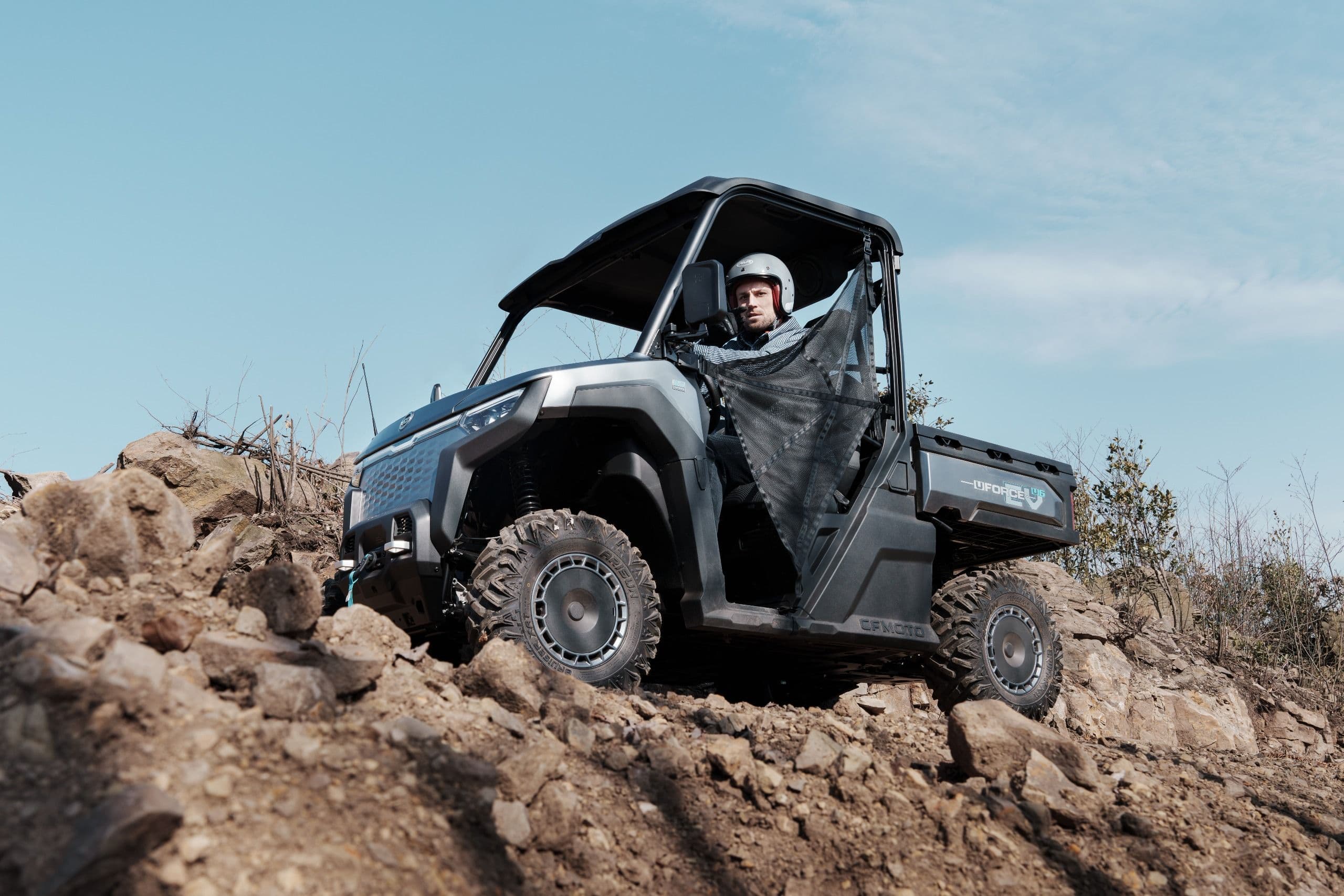 Gray UTV climbs a rocky, dirt hill with a driver on a clear day.